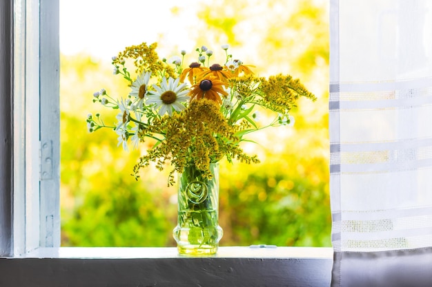 Een prachtig boeket wilde bloemen op een witte vensterbank bij een open raam met een wit gordijn in een landhuis op een zomeravond