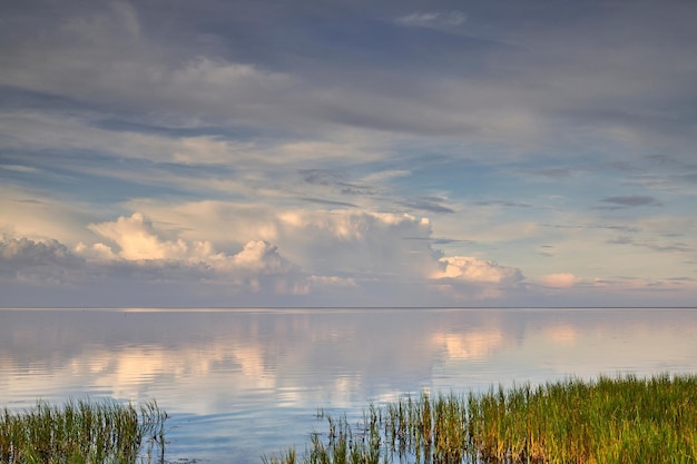 Een prachtig kalm en rustig uitzicht op het meerwater met een bewolkte luchtreflectie en groen gras aan de oever het landschap van een magische horizon met kopieerruimte buiten in de natuur of een rustige omgeving