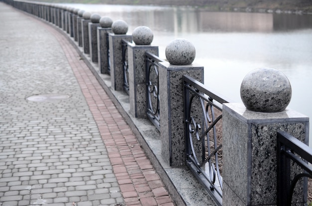 Een prachtige granieten omheining met gesmede metalen delen en decoratieve ballen als decoratie. het hek is langs de dijk van de straat gebouwd