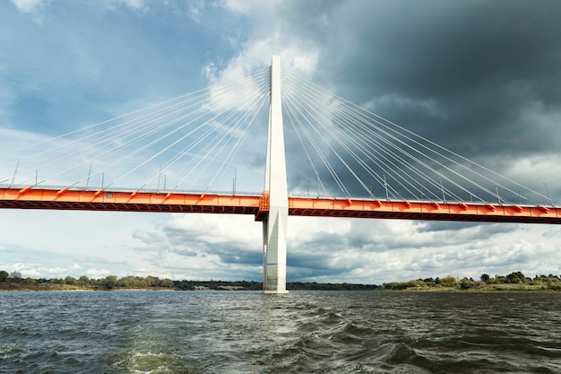 Een prachtige tuibrug over de rivier tegen de achtergrond van een sombere bewolkte hemel. Prachtig landschap.