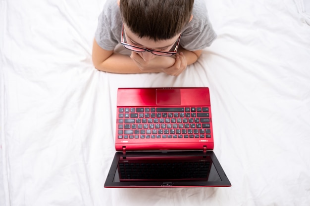 Een preteen jongen liggend op een bed, surfen op internet en typen in zijn blog, kind bloggen concept