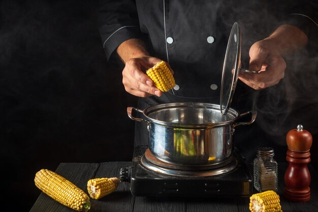 Een professionele chef-kok kookt maïs Close-up van een chef-kok is een hand tijdens het koken in de keuken van een restaurant Gratis advertentieruimte