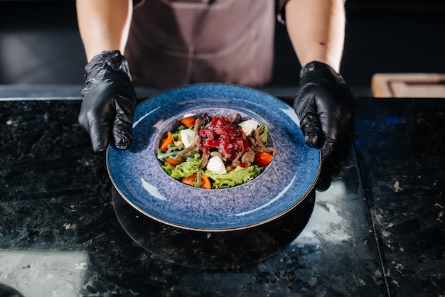 Een professionele chef-kok serveert een vers bereide salade van tomaat en kalfsgroenten met saus in een gastronomisch restaurant close-up gourmet