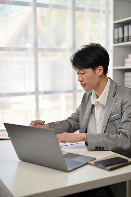 Een professionele en gefocuste Aziatische zakenman die bedrijfsrapporten leest aan zijn bureau