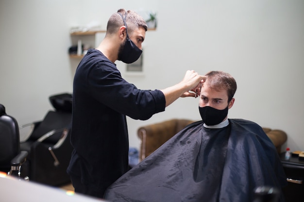 Een professionele kapper die een beschermend masker draagt dat het haar naar een klant knipt tijdens het coronavirus