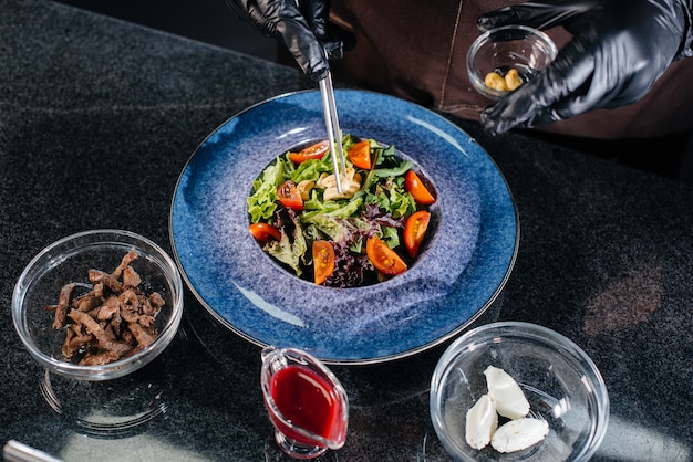 Een professionele kok bereidt in een modern en stijlvol restaurant een heerlijke frisse salade van groene groenten en sappig kalfsvlees. koken in een restaurant.