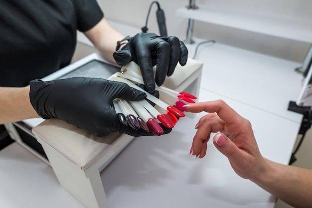 Een professionele nagelverlengingsmeester kiest een kleur voor zijn cliënt tijdens een epidemie Gekleurd manicureconcept voor cliënt