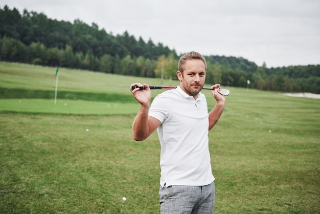 Foto een professionele speler staat op de golfbaan en houdt de metalen stok achter zijn rug