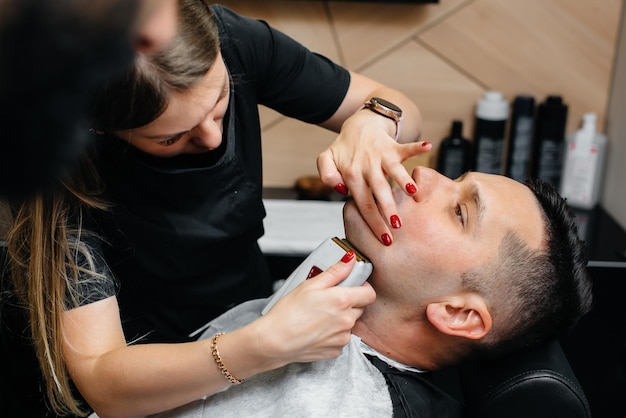 Een professionele stylist in een moderne stijlvolle kapperszaak scheert en knipt het haar van een jonge man. Schoonheidssalon, kapsalon.