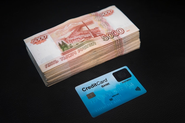 Een prop geld van Russische roebels en een plastic bankkaart liggen op een zwarte achtergrond Kaart en Russische roebels bankbiljetten.