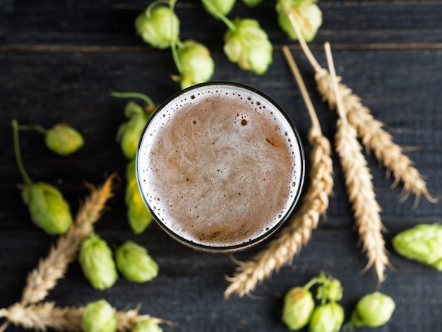 Een pul bier op een houten tafel met groene hop en korenaren