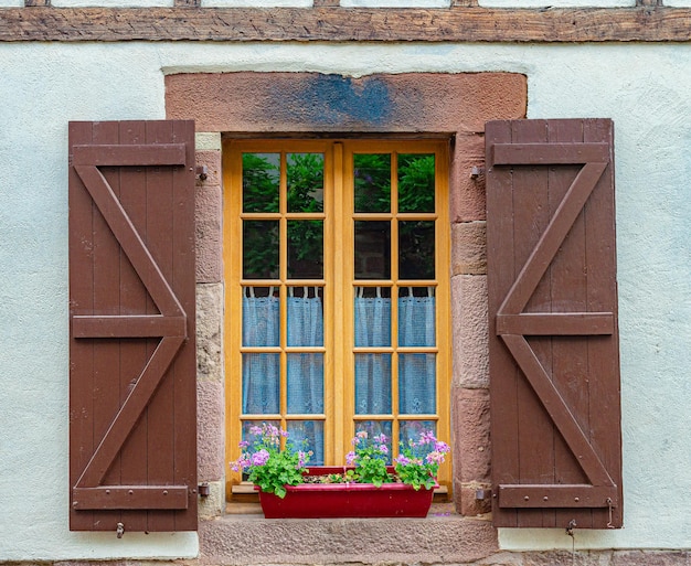 Een raam met een rode bloembak en een raam met een raam met een houten luik.