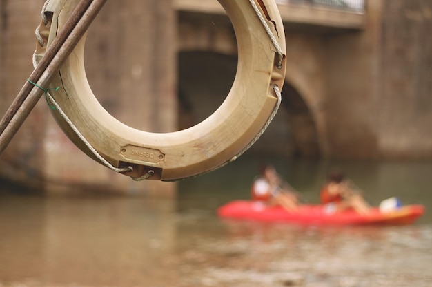 Een reddingsboei hangt aan een touw in een rivier met op de achtergrond twee mensen in een dubbele kano