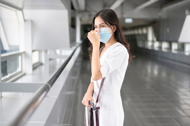 Een reizende vrouw draagt een beschermend masker op de internationale luchthaven, reist onder Covid-19 pandemie, veiligheidsreizen, sociaal afstandsprotocol, nieuw normaal reisconcept.