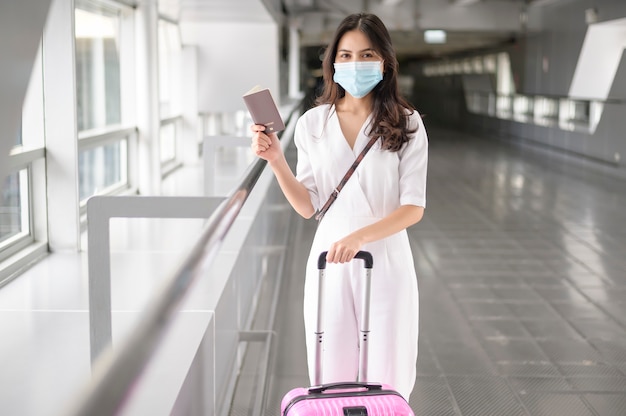 Een reizende vrouw draagt een beschermend masker op de internationale luchthaven, reist onder Covid-19 pandemie, veiligheidsreizen, sociaal afstandsprotocol, nieuw normaal reisconcept.