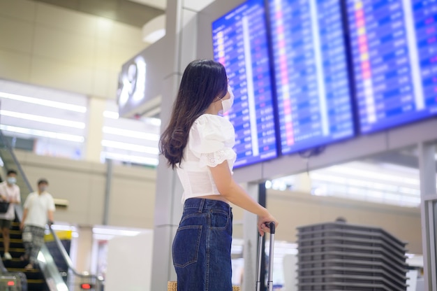 Een reizende vrouw draagt een beschermend masker op de internationale luchthaven, reist onder Covid-19 pandemie, veiligheidsreizen, sociaal afstandsprotocol