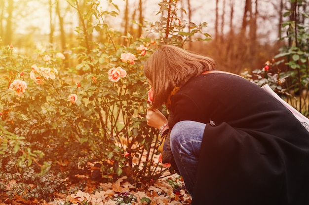 Een reizigersvrouw in mode-herfstkleding die aan de roze bloemen in het herfstpark snuffelt. lokaal reisconcept. gloed