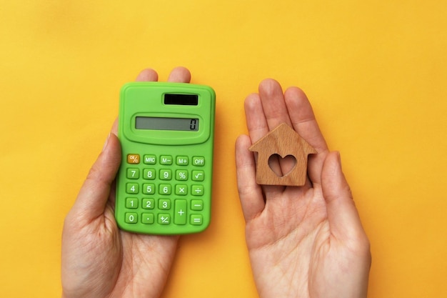 Een rekenmachine en een houten huis in iemands hand Het symbool van het kopen van een huis