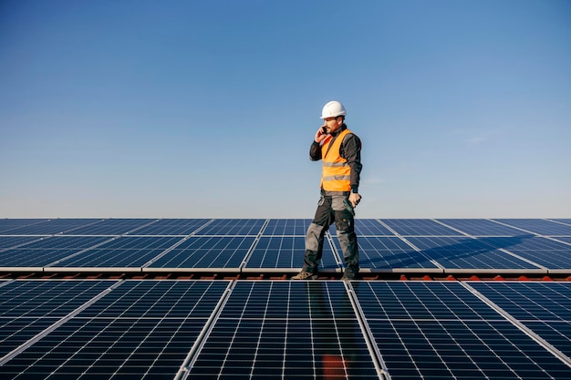 Een reparateur aan het telefoneren terwijl hij op een dak staat omringd door zonnepanelen