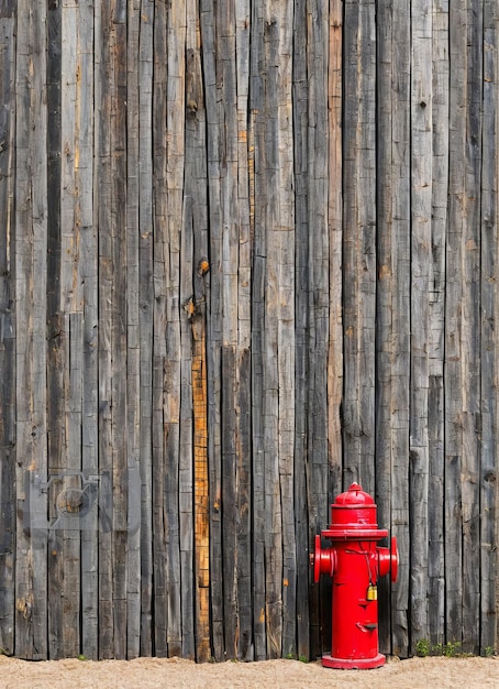 Een rode brandkraan staat voor een houten hek.