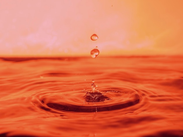 Een rode druppel druppelt in het water en creëert spatten van verschillende vormen, door de spatten worden golven op het water gecreëerd, het concept van een vloeibare plons, de substantie is roze geverfd