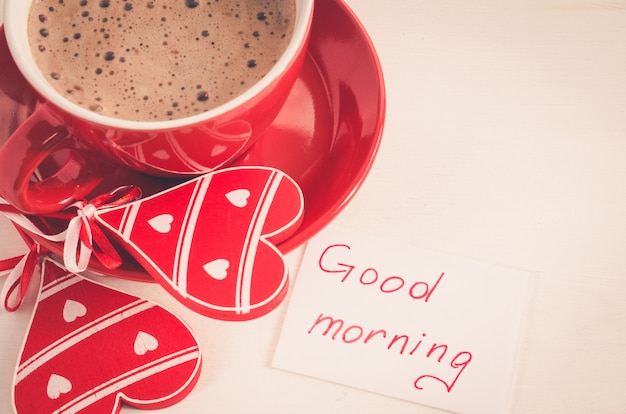 Een rode kop cappuccino met houten hart en notities Goedemorgen.