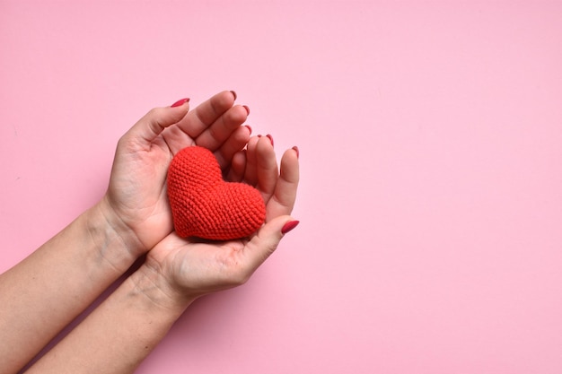 Een rood gebreid hart in de handen van een meisje met een mooie manicure op een roze achtergrond Liefde Orgaandonatie Zwangerschap Valentijnsdag