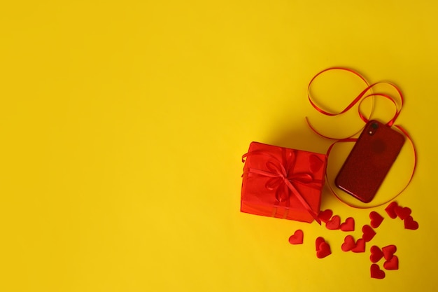 Een rood geschenk en harten op een gele achtergrond Afbeelding voor Valentijnsdag 14 februari