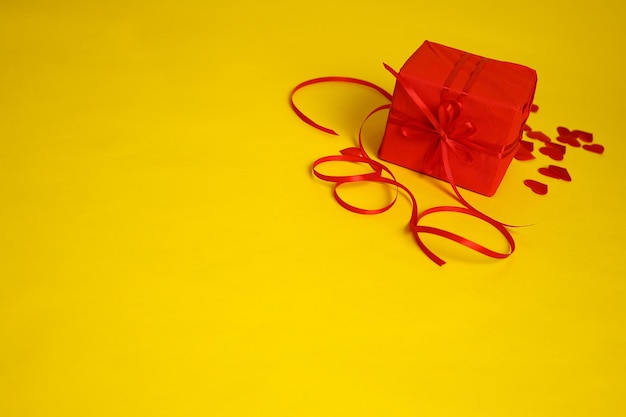 Een rood geschenk en harten op een gele achtergrond Afbeelding voor Valentijnsdag 14 februari