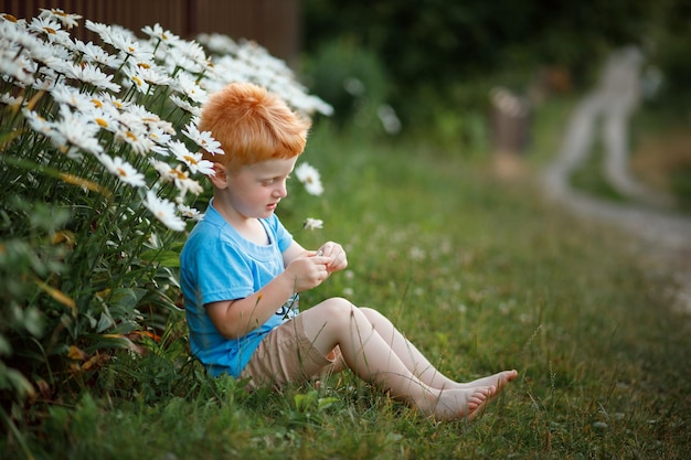Een roodharig jongetje speelt met bloemen in de buurt van zijn huis en wacht op zijn moeder