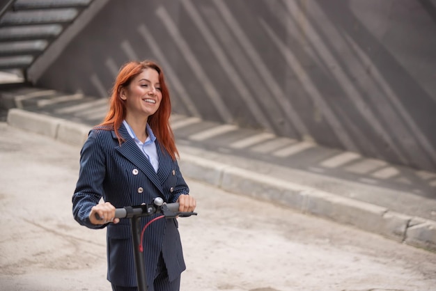 Een roodharig meisje in een jas en broek rijdt op een elektrische scooter langs de muur Een zakenvrouw in een broekpak en rode hoge hakken rijdt door de stad in een moderne auto Kantoormedewerker Kledingvoorschrift