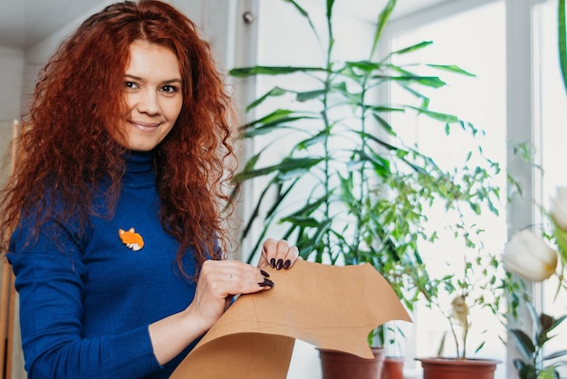 Een roodharige naaister van middelbare leeftijd buigt een patroon doormidden Modeontwerper werkt thuis