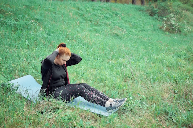 Een roodharige vrolijke vrouw in sportkleding sport in het park om overtollig gewicht en een gezonde levensstijl te verliezen