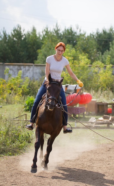 Een roodharige vrouw met een bril berijdt een paard in de natuur