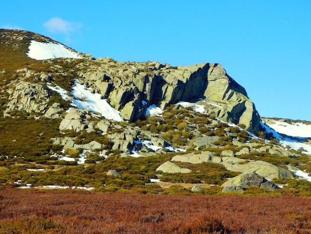 Een rotsachtig landschap met sneeuw op de grond en een berg op de achtergrond.