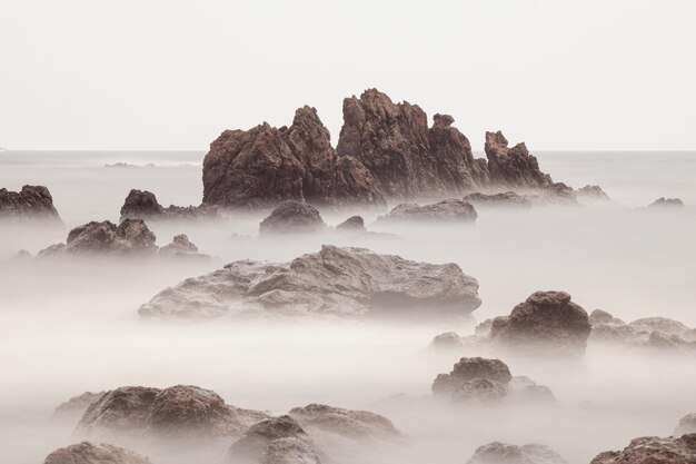 Een rotsachtig strand met een mistige lucht en rotsen op de voorgrond.