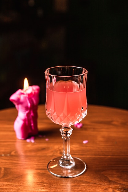 Een roze cocktail in een prachtig kristalglas, een kaars, op een houten tafel, aan de bar.