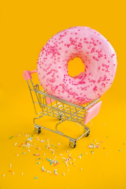 Een roze donut met roze hagelslag zit in een winkelwagentje.