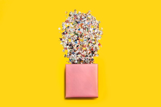 Een roze geschenkdoos met confetti op een gele achtergrond