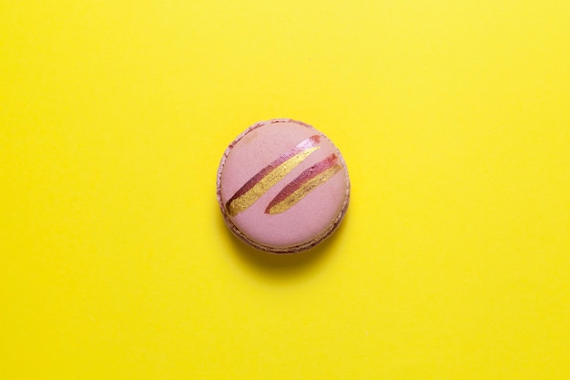 Een roze macaron of macaron met glanzende gouden strepen ligt op geel