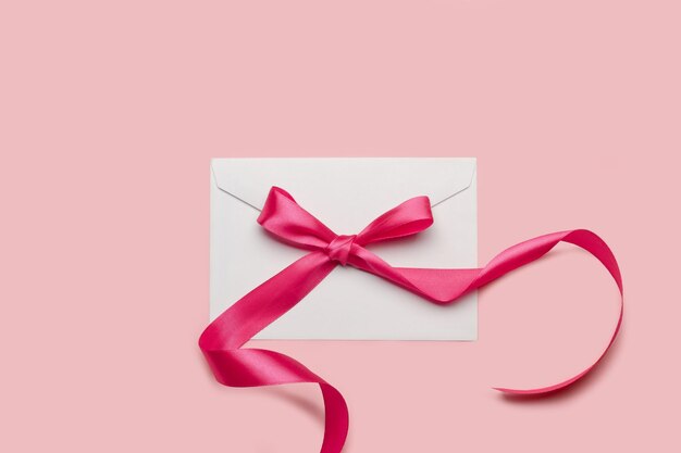 Een roze strik op een witte envelop op een roze achtergrond
