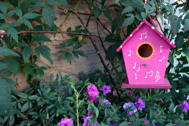 Een roze vogelhuis hangt op een boom die door petuniabloemen wordt omringd.