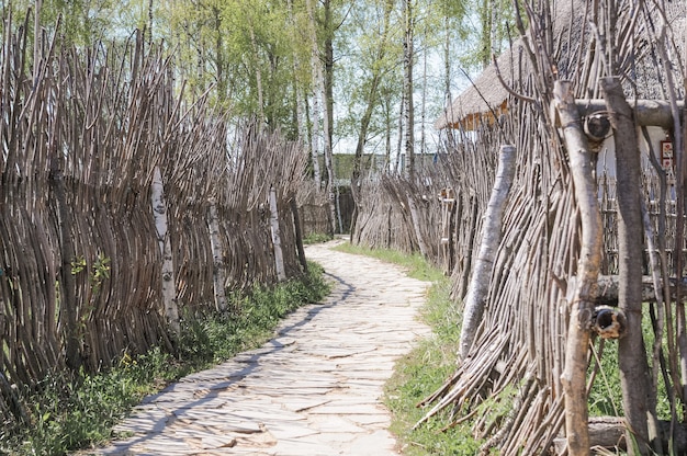 Een rustiek pad geplaveid met steen en een houten hek gemaakt van natuurlijke natuurmaterialen van boomtakken. zorg voor de ecologie van de natuur en plasticvrij. russisch plattelandsdorp