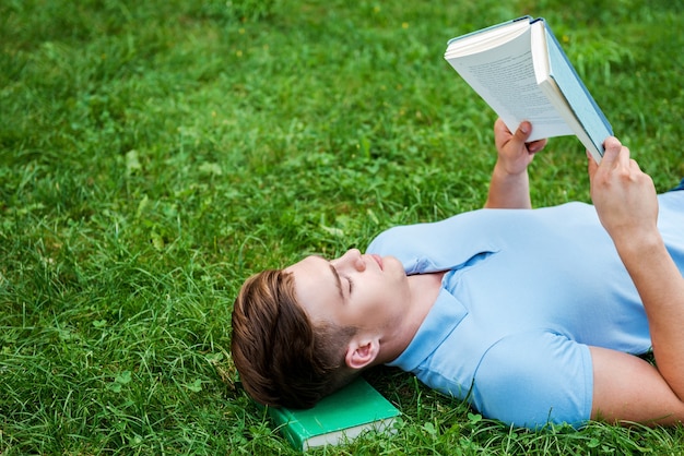 Een rustige plek vinden om te lezen. Bovenaanzicht van een knappe jongeman die een boek leest terwijl hij op het gras ligt met een laptop