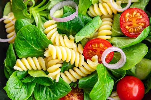 Een salade van pasta, tomaten en uien met daarop een rode ui.