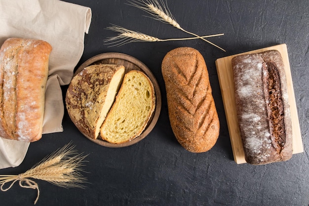 Een samenstelling van vers zelfgebakken brood van verschillende vormen op een zwarte achtergrond met korenaren