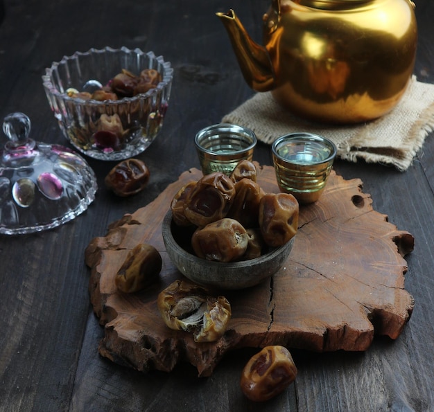 Een schaal met dadels staat op een houten tafel naast een theepot met een gouden deksel.