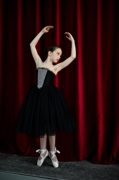 Een schattig ballerinameisje in een zwarte jurk op een rode achtergrond Art Dance Beauty