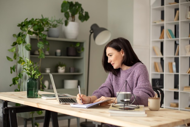 een schattig brunette meisje in een lila trui zit aan een tafel met een laptop die aantekeningen maakt