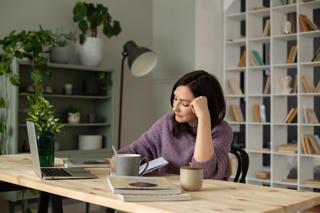 een schattig brunette meisje in een lila trui zit aan een tafel met een laptop die aantekeningen maakt